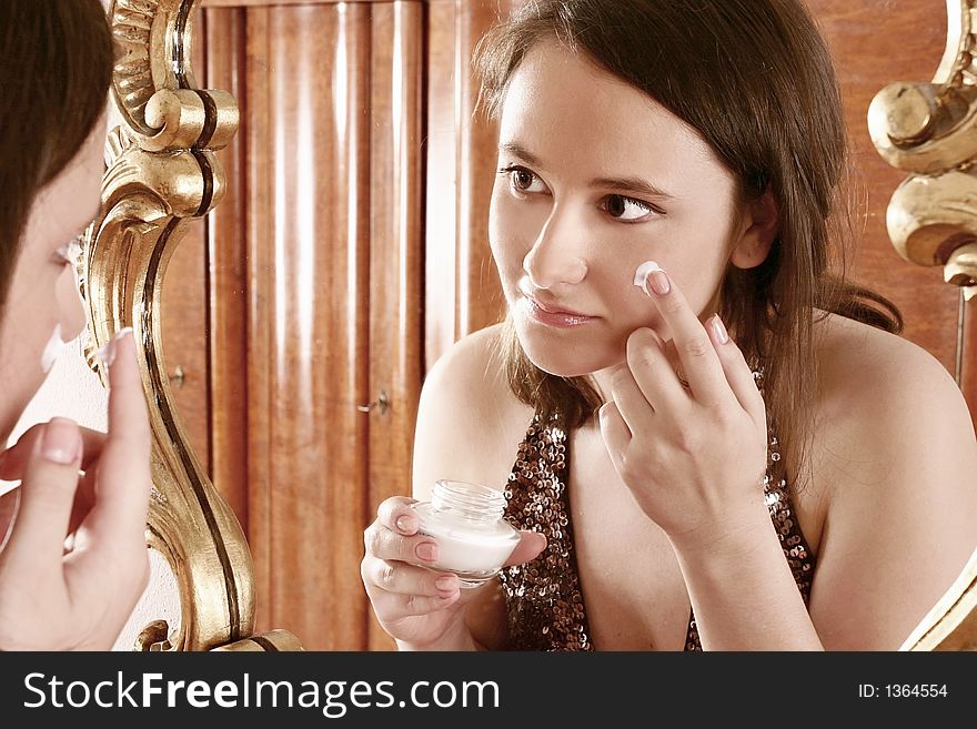 Auburn-haired girl, young woman putting cream in front of  a mirror