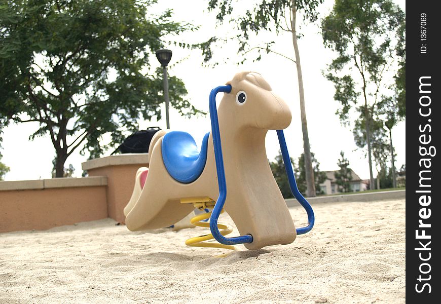 Beige kiddy horse with blue seat in a sand playground. Beige kiddy horse with blue seat in a sand playground