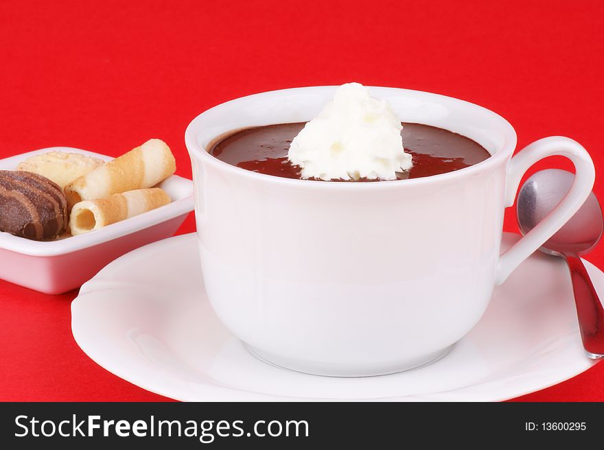 A cup of hot chocolate with whipped cream and some cookies. Studio shot over red background. Shallow DOF.