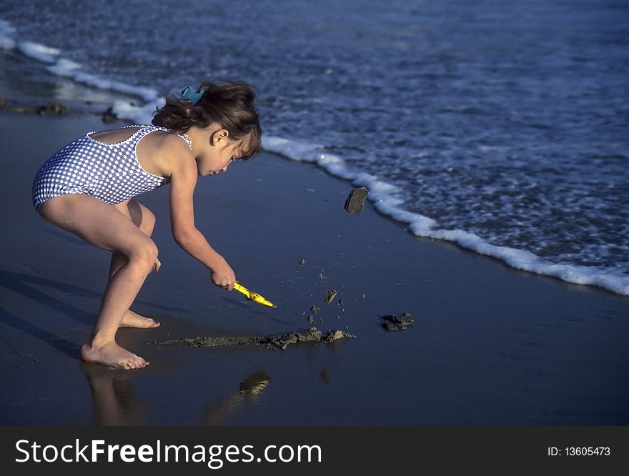 Little girl shoveling sand with a toy shovel on a beach. Little girl shoveling sand with a toy shovel on a beach