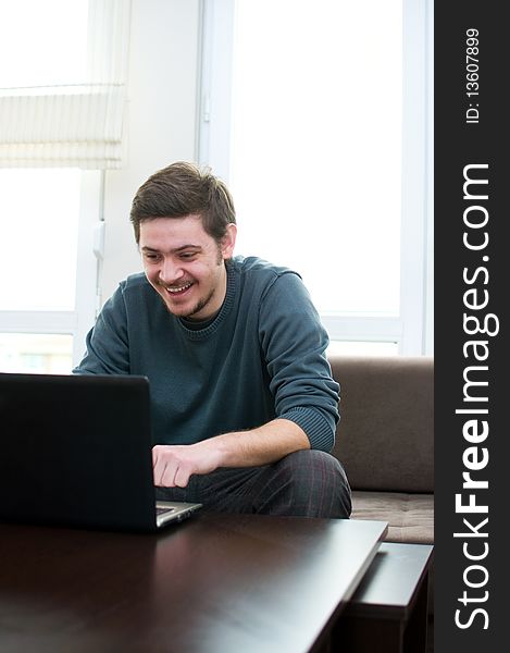 Portrait of a smiling man working on a laptop at home sitting on the couch. Portrait of a smiling man working on a laptop at home sitting on the couch