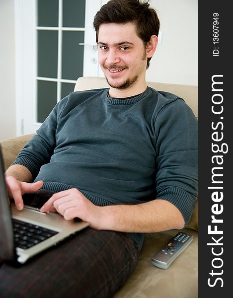 Portrait of a smiling man working on a laptop at home sitting on the couch. Portrait of a smiling man working on a laptop at home sitting on the couch