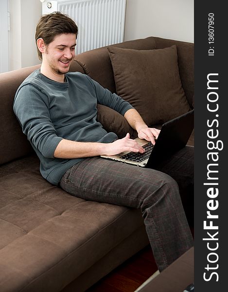 Portrait of a smiling man working on a laptop at home sitting on the couch. Portrait of a smiling man working on a laptop at home sitting on the couch