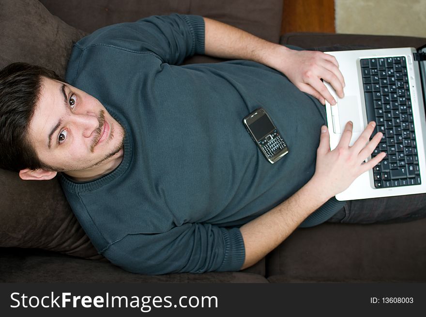 Portrait of a smiling man working on a laptop at home sitting on the couch. Portrait of a smiling man working on a laptop at home sitting on the couch