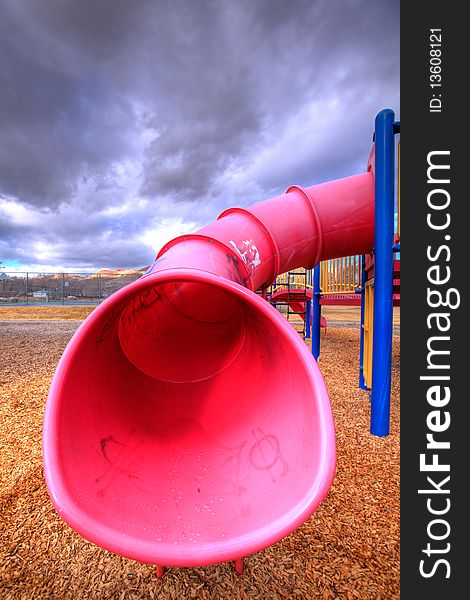 A child's playground set tube slide with wood-chips about on the ground.