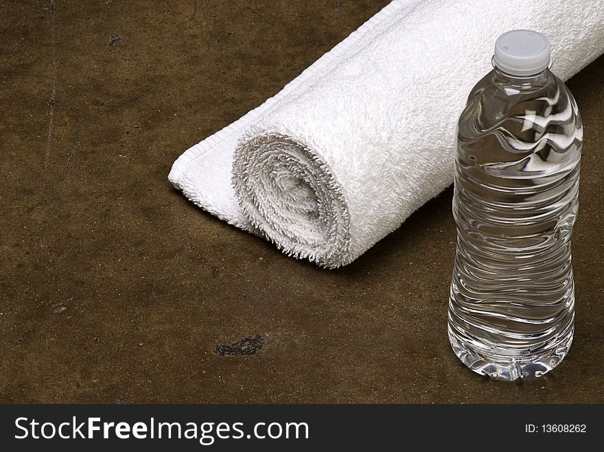 Rolled up white towel with bottle of water isolated on grunge textured background