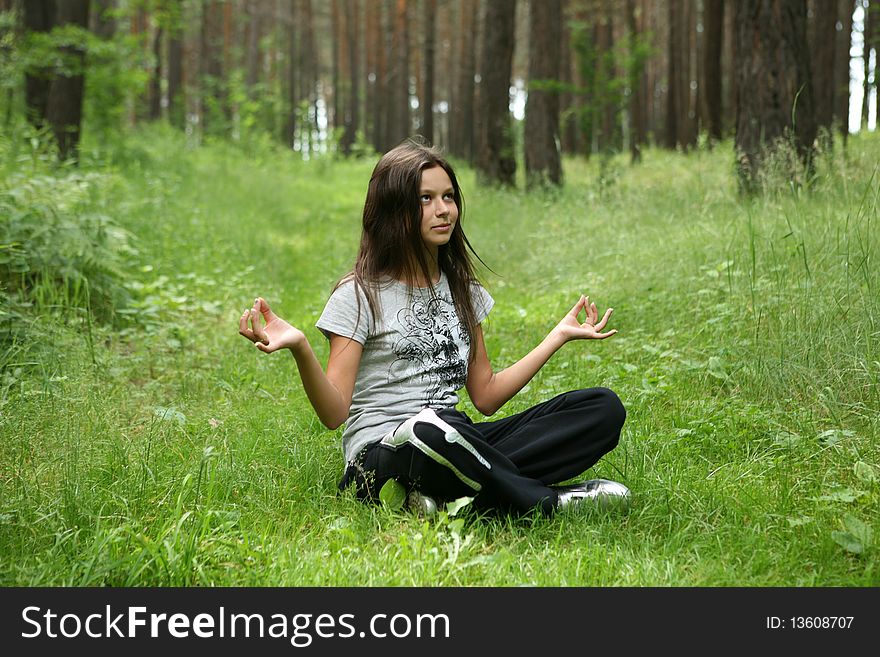 The girl doing exercise on a green grass in a wood. The girl doing exercise on a green grass in a wood