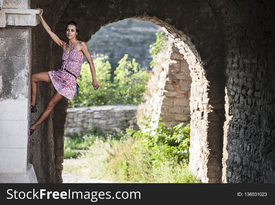 The girl climbs the stone wall. A woman in a summer dress climbs the wall of an old destroyed building. Brick fence. The climber is hanging on the city building. Strengthening the ruined castle