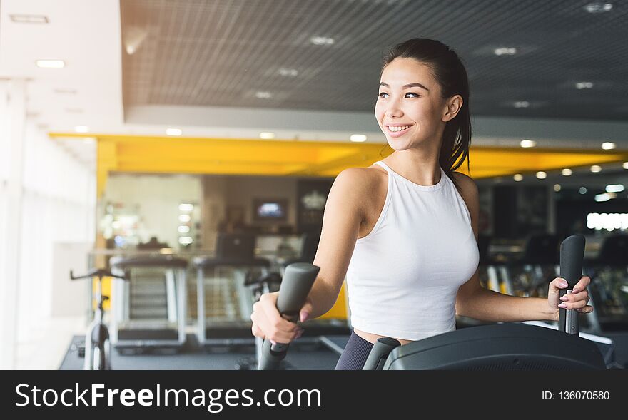 Woman exercising at elliptical trainer in gym