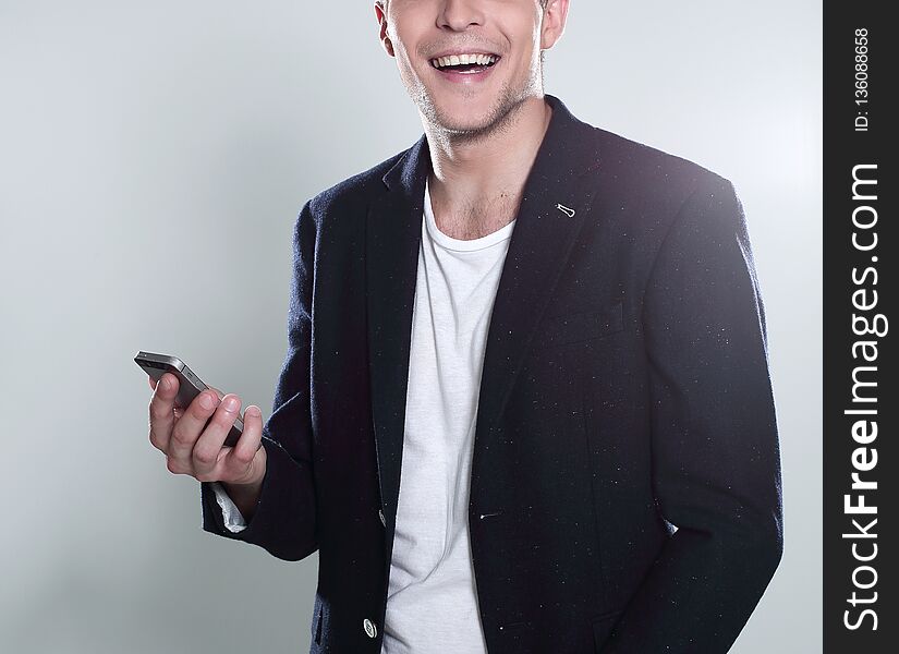 Receiving nice messages. Handsome young man in jacket looking on his smart phone and smiling while standing against grey background. Receiving nice messages. Handsome young man in jacket looking on his smart phone and smiling while standing against grey background