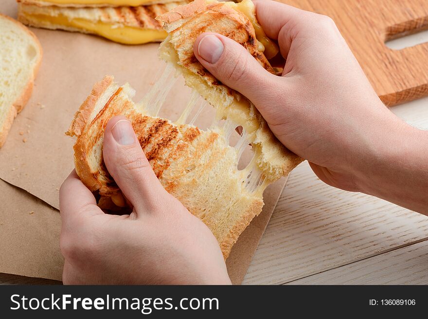 Man tearing a sandwich in half. Crunchy grilled crust and stretchy melted cheese. Mouthwatering and delicious food.