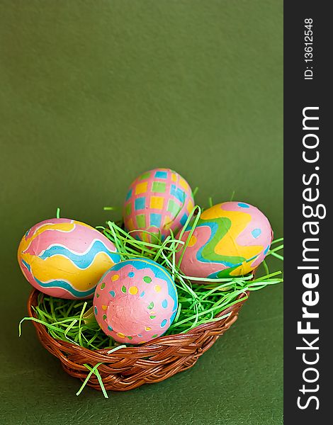 Colored Easter eggs in a basket on green background