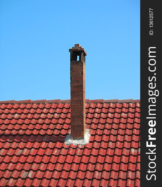Red brick chimney on tile roof over blue sky
