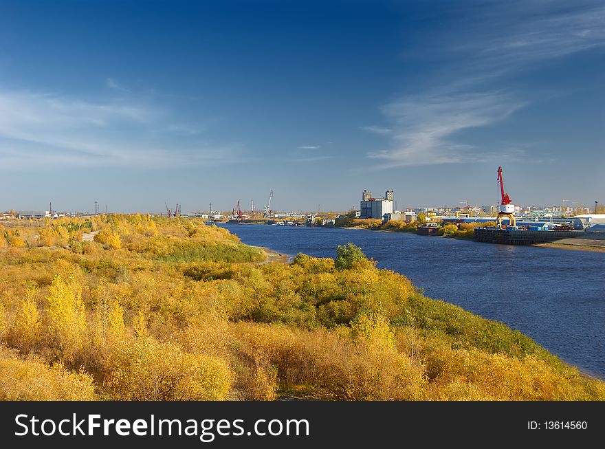 View of city port and river with coast covered autumn trees with multicolor foliage