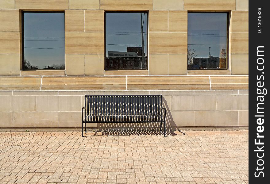 Image of a public bench under three windows on an interlocking brick surface. Image of a public bench under three windows on an interlocking brick surface