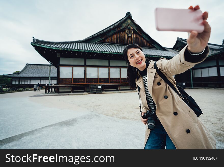 Smiling hipster woman taking selfie photo in nijo jo fitland castle on the background kyoto japan. young girl traveler using smartphone camera app make self portrait. japanese tradition building. Smiling hipster woman taking selfie photo in nijo jo fitland castle on the background kyoto japan. young girl traveler using smartphone camera app make self portrait. japanese tradition building