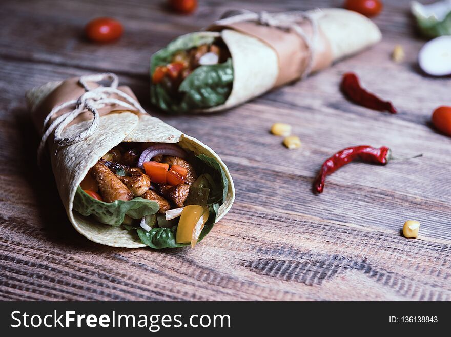 Traditional mexican tortilla wrap with vegetables and grilled chicken meat on wood table