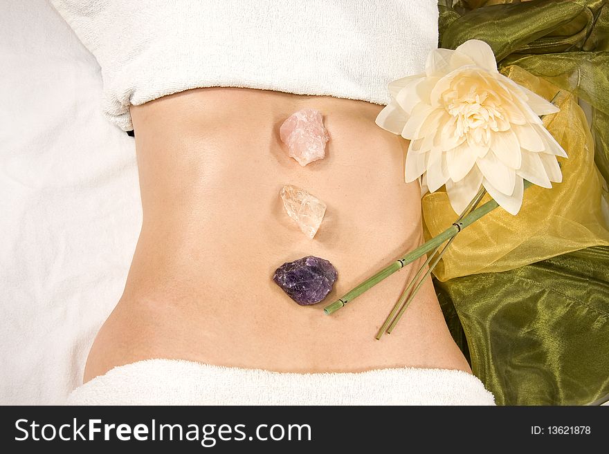 A wellness composition showing the abdomen of a natural mature woman, stones, a flower and a silk scarf