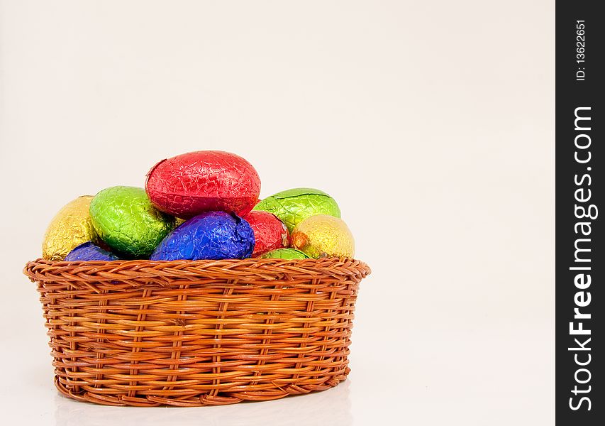 Colorful easter eggs wrapped in shiny foil in wicker basket white background. Colorful easter eggs wrapped in shiny foil in wicker basket white background