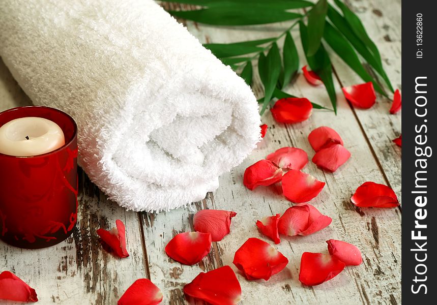 Spa composition of towel, candle and red petals on wooden