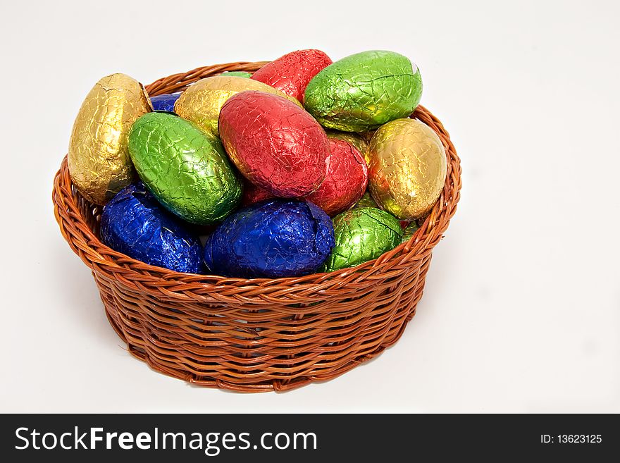 Colorful easter eggs wrapped in shiny foil in wicker basket white background. Colorful easter eggs wrapped in shiny foil in wicker basket white background