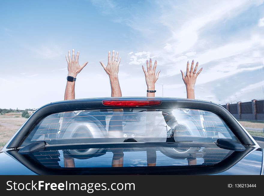 Group of happy young people waving from a convertible car