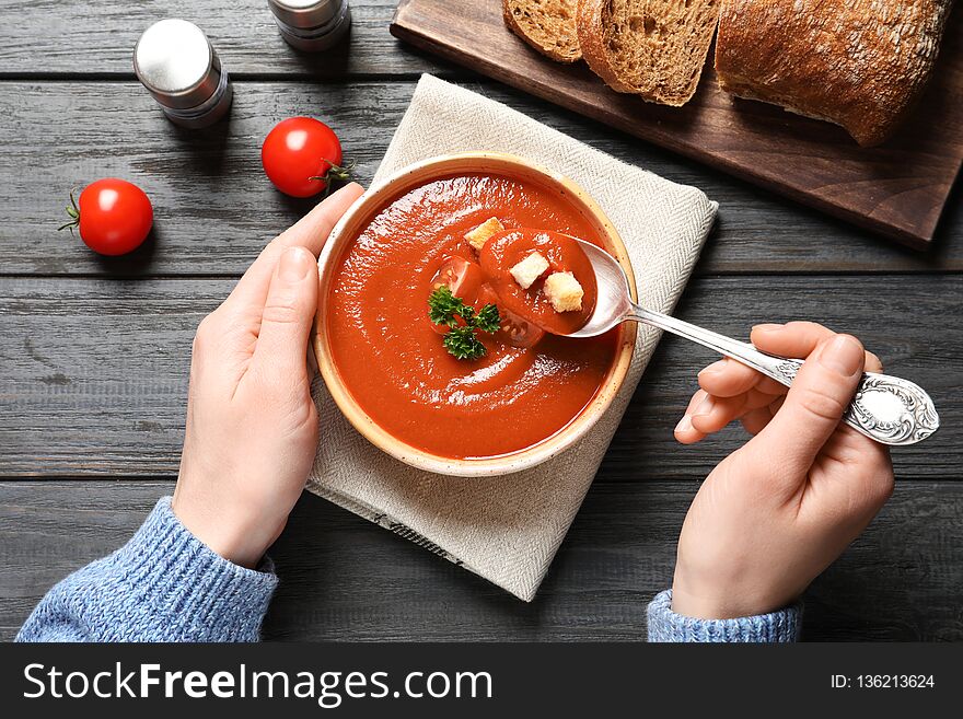 Woman eating fresh homemade tomato soup at wooden table