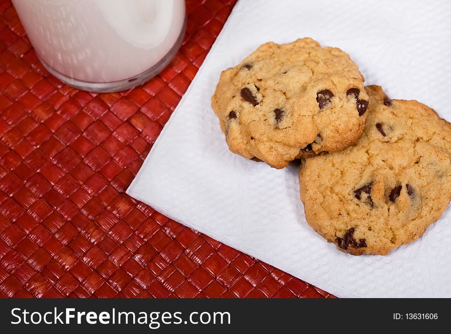 Chocolate chip cookies and glass of milk on red woven placemat. Chocolate chip cookies and glass of milk on red woven placemat