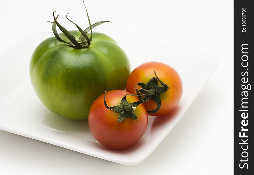 Green and red tomatoes on white plate