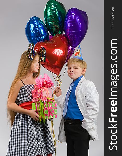 Beautiful boy and girl standing side by side with gifts and balloons in their hands. Beautiful boy and girl standing side by side with gifts and balloons in their hands
