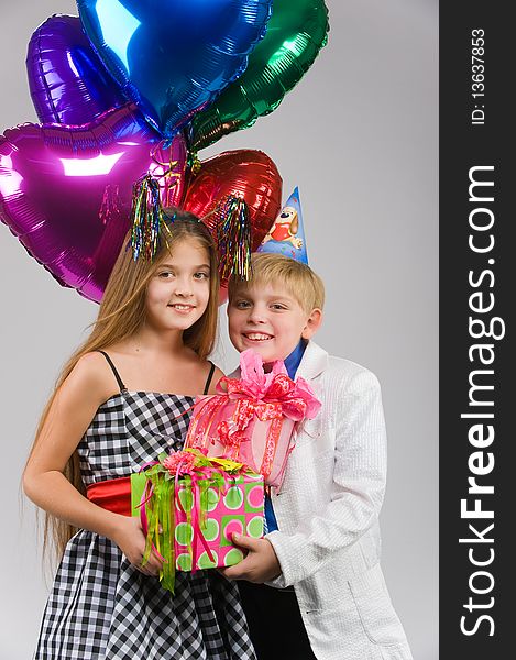 Beautiful boy and girl standing side by side with gifts and balloons in their hands. Beautiful boy and girl standing side by side with gifts and balloons in their hands