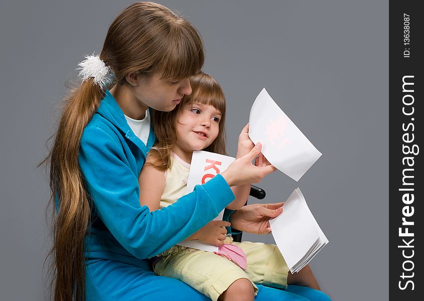 A young girl in a blue suit sitting with a child in her arms and teaches her to read. A young girl in a blue suit sitting with a child in her arms and teaches her to read