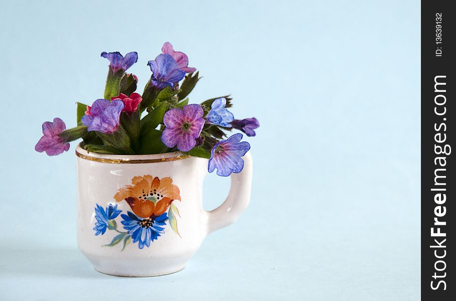 Small bouquet of blue lungwort  (pulmonaria obscura) in a painted cup vase. Small bouquet of blue lungwort  (pulmonaria obscura) in a painted cup vase.