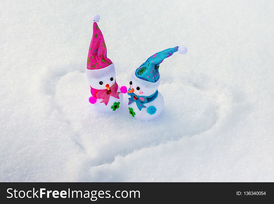 Toy snowmen are in the snow on which the heart is painted. Congratulations on Valentine`s Day_