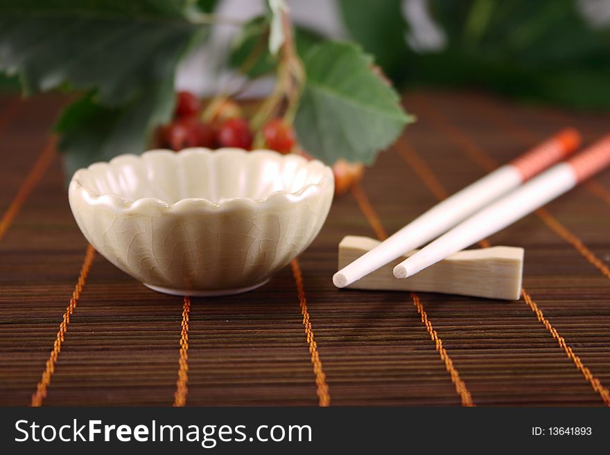 Cup and chopsticks on a wooden napkin against plants. Cup and chopsticks on a wooden napkin against plants