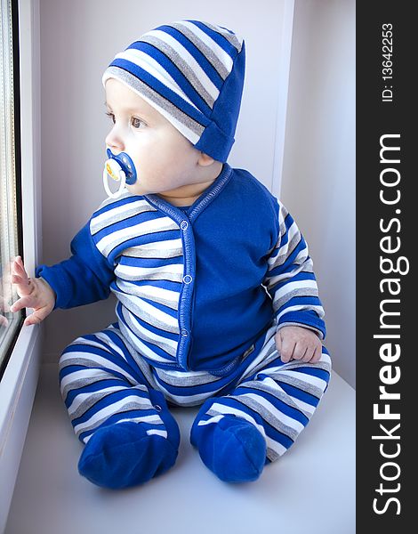 The baby of 6-7 months in a suit in a strip sits and looks out of the window