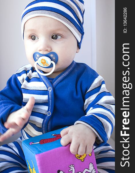 The baby of 6-7 months in a dark blue suit sits with a cube in hands