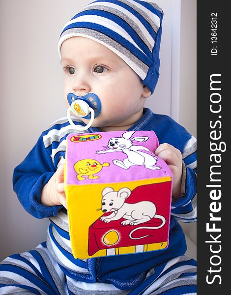 The baby of 6-7 months in a dark blue suit sits with a cube in hands