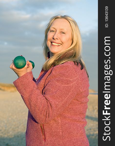 A colour portrait photo of a beautiful happy smiling older lady in her sixties exercising with dumbells on the beach. A colour portrait photo of a beautiful happy smiling older lady in her sixties exercising with dumbells on the beach.