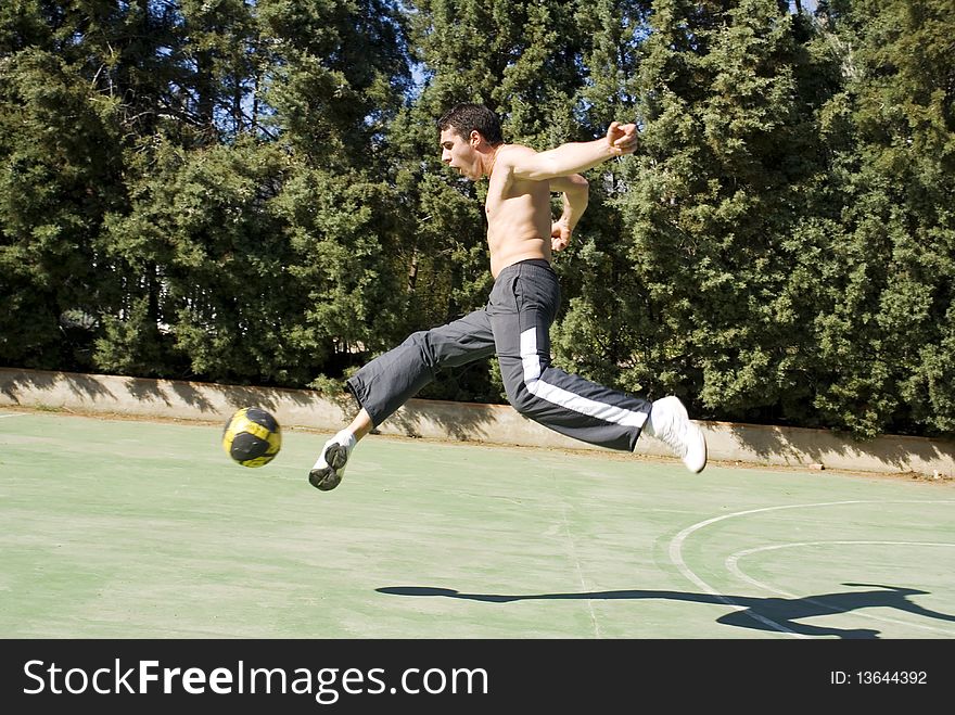 A young man playing football kicking the ball. A young man playing football kicking the ball