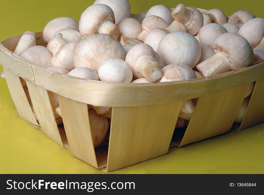 A lot of champignons in a wicker basket on yellow background