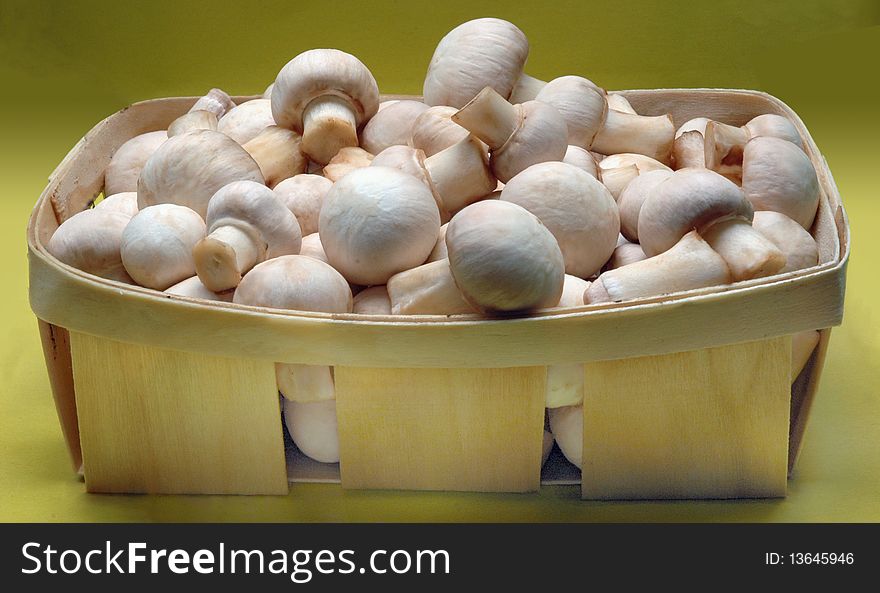 A lot of champignons in a wicker basket on yellow background