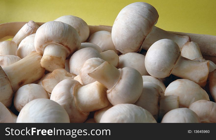 A lot of champignons in a wicker basket on yellow background