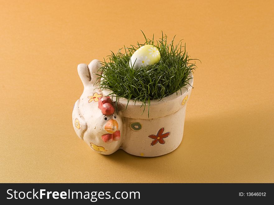 Clay pot in the shape of chicken with grass and egg on the top on gold background!. Clay pot in the shape of chicken with grass and egg on the top on gold background!