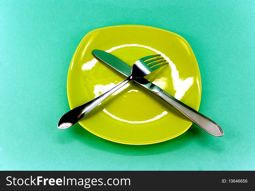 Plate, knife and fork against green background. Plate, knife and fork against green background