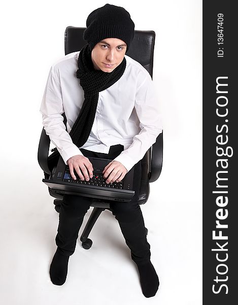 Teenager, wearing a knitted cap, in an office chair holding a computer aginst a white background. Teenager, wearing a knitted cap, in an office chair holding a computer aginst a white background.