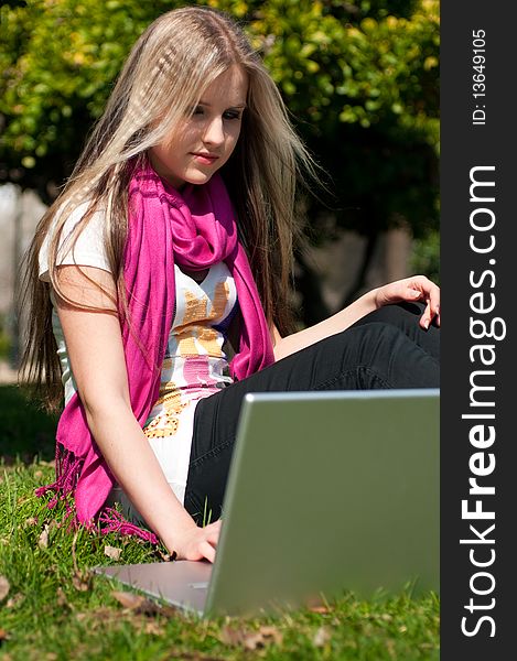 A beautiful attractive blond girl with a laptop in a park. A beautiful attractive blond girl with a laptop in a park