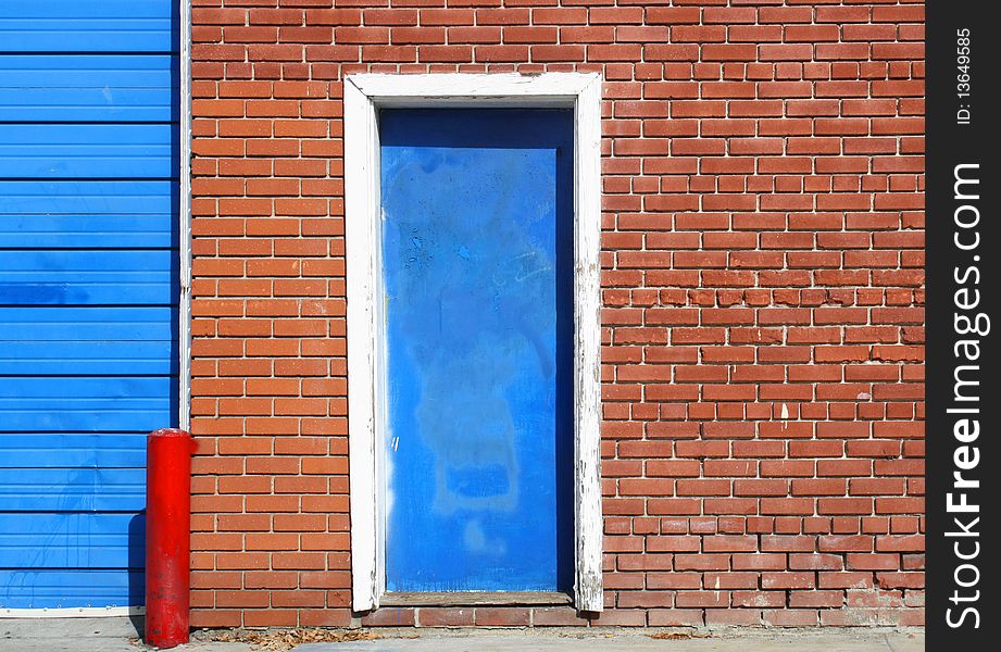 An old blue door in an urban red, brick wall, is seen along a sidewalk. An old blue door in an urban red, brick wall, is seen along a sidewalk.