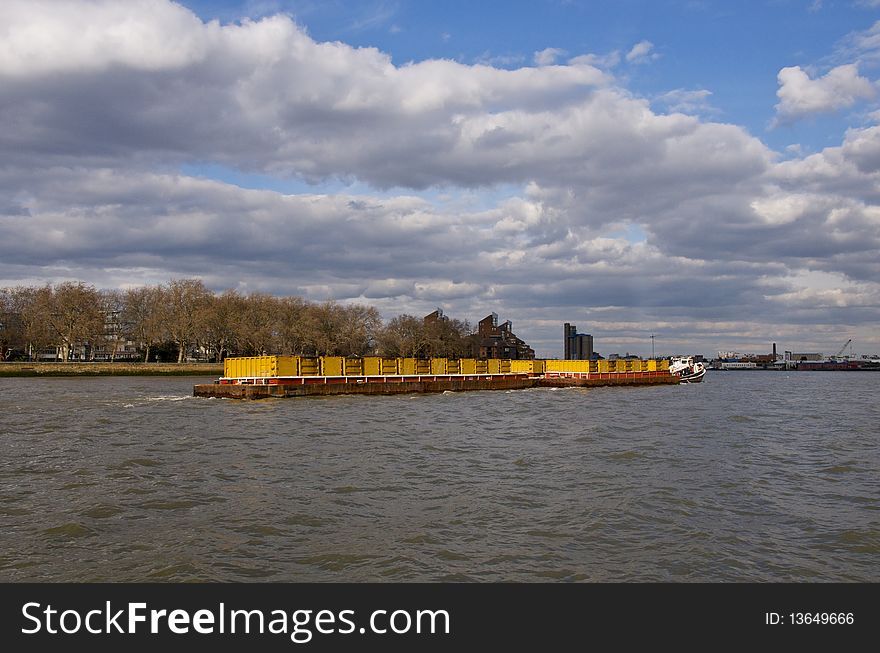 A container barge with cargo on the Thames River in London with beautiful sky. A container barge with cargo on the Thames River in London with beautiful sky