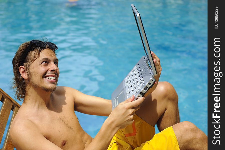 Attractive man uses his laptop while tanning poolside. Attractive man uses his laptop while tanning poolside